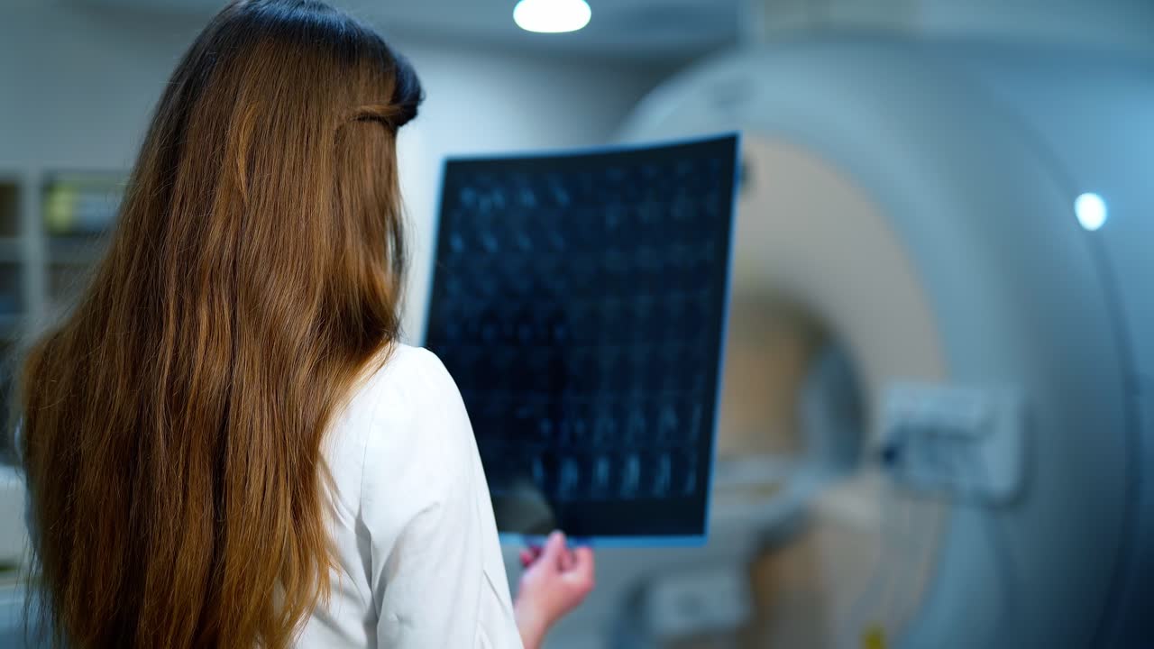 Medic examines x-ray in a contemporary clinic. Backside view of a female doctor holding radiogram picture. Medical concept.