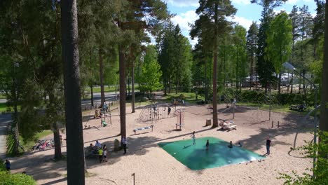 aerial dolly in trees above children playing jumping on sandy playground