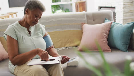 senior african american woman measuring pressure and taking notes at home