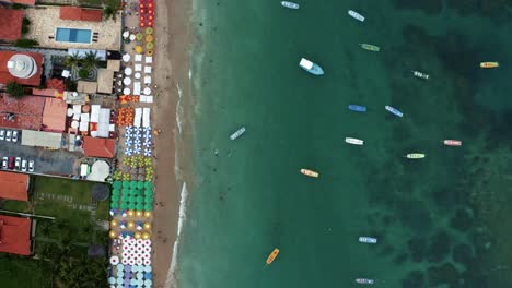 Vogelperspektive-Von-Oben-Nach-Unten-Bewegte-Luftaufnahme-Des-Berühmten-Porto-De-Galinhas-Oder-Chicken-Port-Beach-In-Pernambuco,-Brasilien-Mit-Bunten-Regenschirmen,-Touristen,-Die-In-Den-Natürlichen-Pools-Schwimmen,-Und-Segelbooten