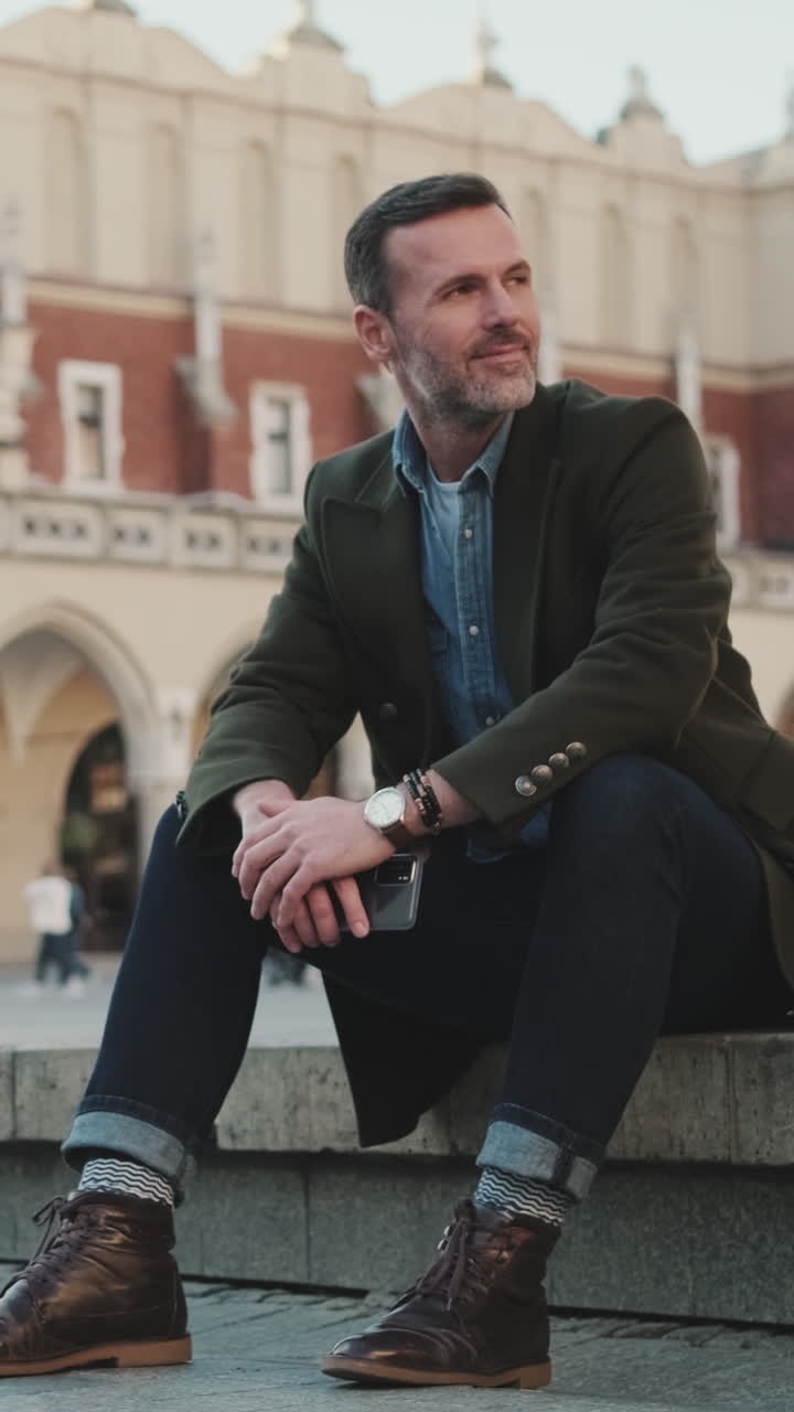Uomo con abiti alla moda seduto in una piazza cittadina