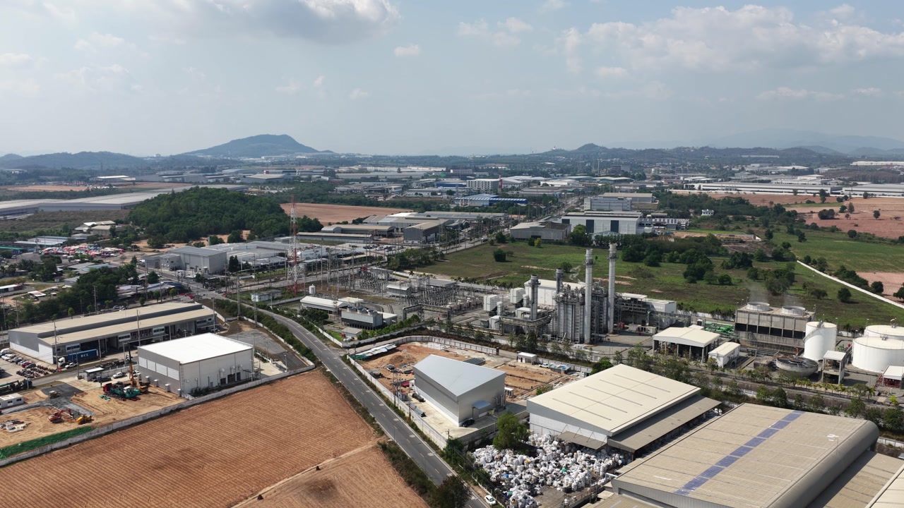 Wide aerial perspective of a sprawling industrial zone, showcasing numerous factories, manufacturing plants, and warehouses interspersed with agricultural land under a partly cloudy sky