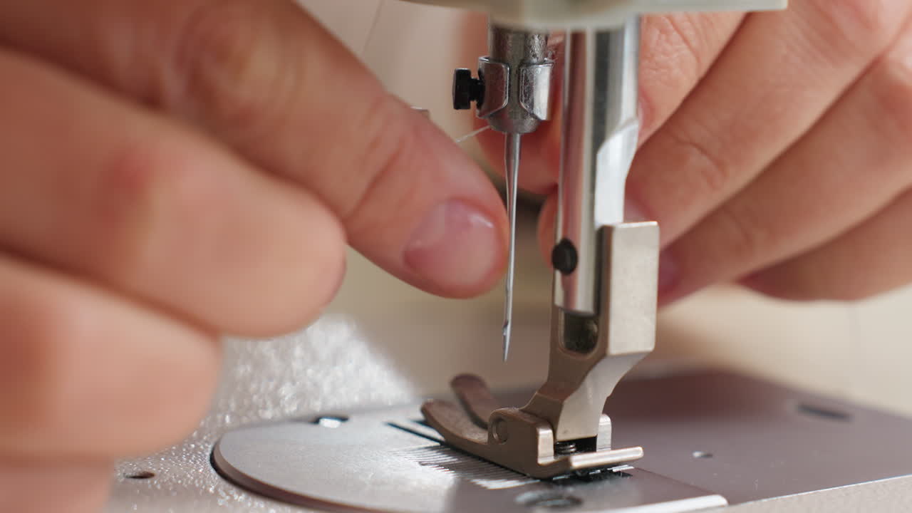Hand of female weaver carefully passing thread through needle on sewing machine, highlighting skillful approach, close up detail, and precise motion in bright minimal workspace, focusing on technique
