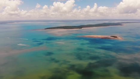 boats sail across a grand expanse of gorgeously tropical blue and green water whilst creamy, white sand beaches sit in the distance on the coast of small islands under sunny, blue skies