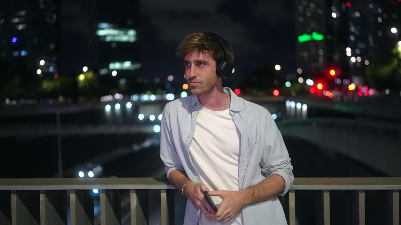 Man with headphones on a bridge at night