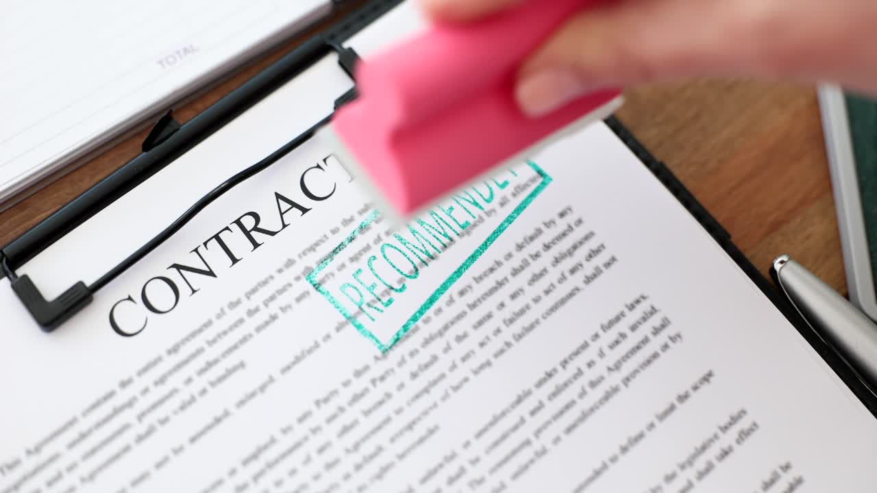 A hand stamping a contract document with "RECOMMENDED"
