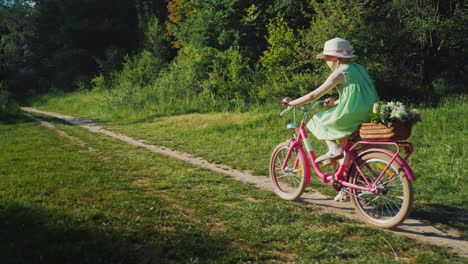 A-Girl-In-A-Green-Summer-Dress-Is-Riding-Along-A-Path-In-The-Forest-Carries-A-Basket-Of-Flowers-Acti