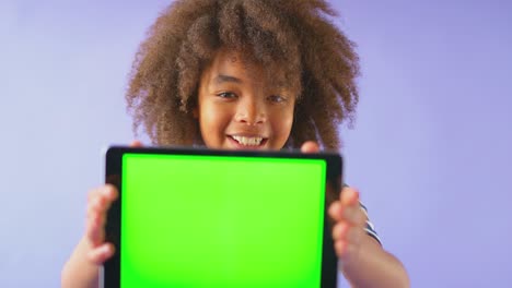 studio shot of smiling boy holding digital tablet with green screen looking at camera against purple studio background - shot in slow motion