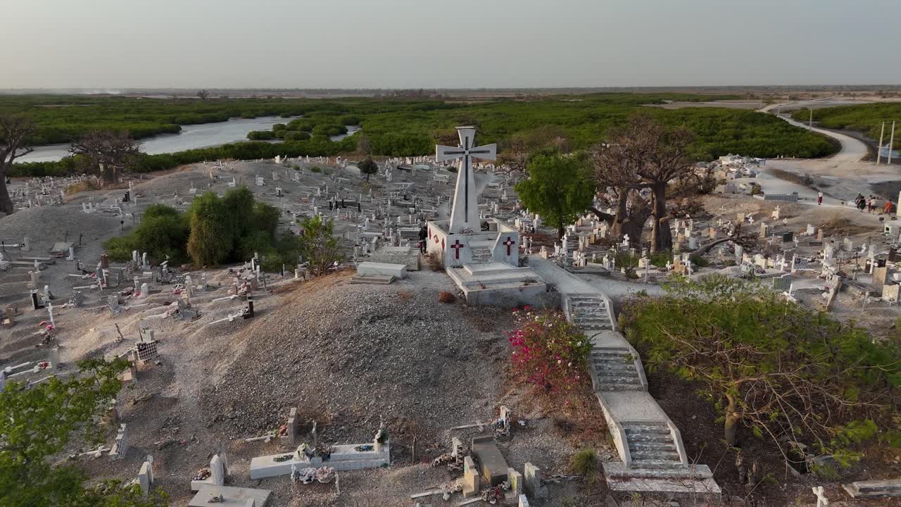 Drone orbit aerial of Joal Fadiouth shell cemetery in Senegal, unique interfaith burial site built entirely on seashells, surrounded by water during sunset