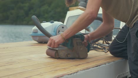 carpenter using belt sander to sand roof planks of wooden boat roof