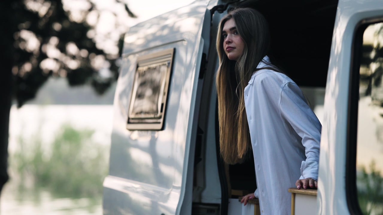 Giovane donna che guarda fuori dal camper nella natura.