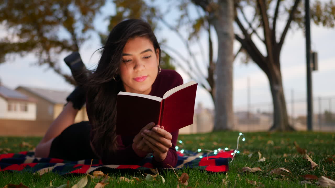 A young female college student studying and reading a literature textbook outdoors on a university school campus