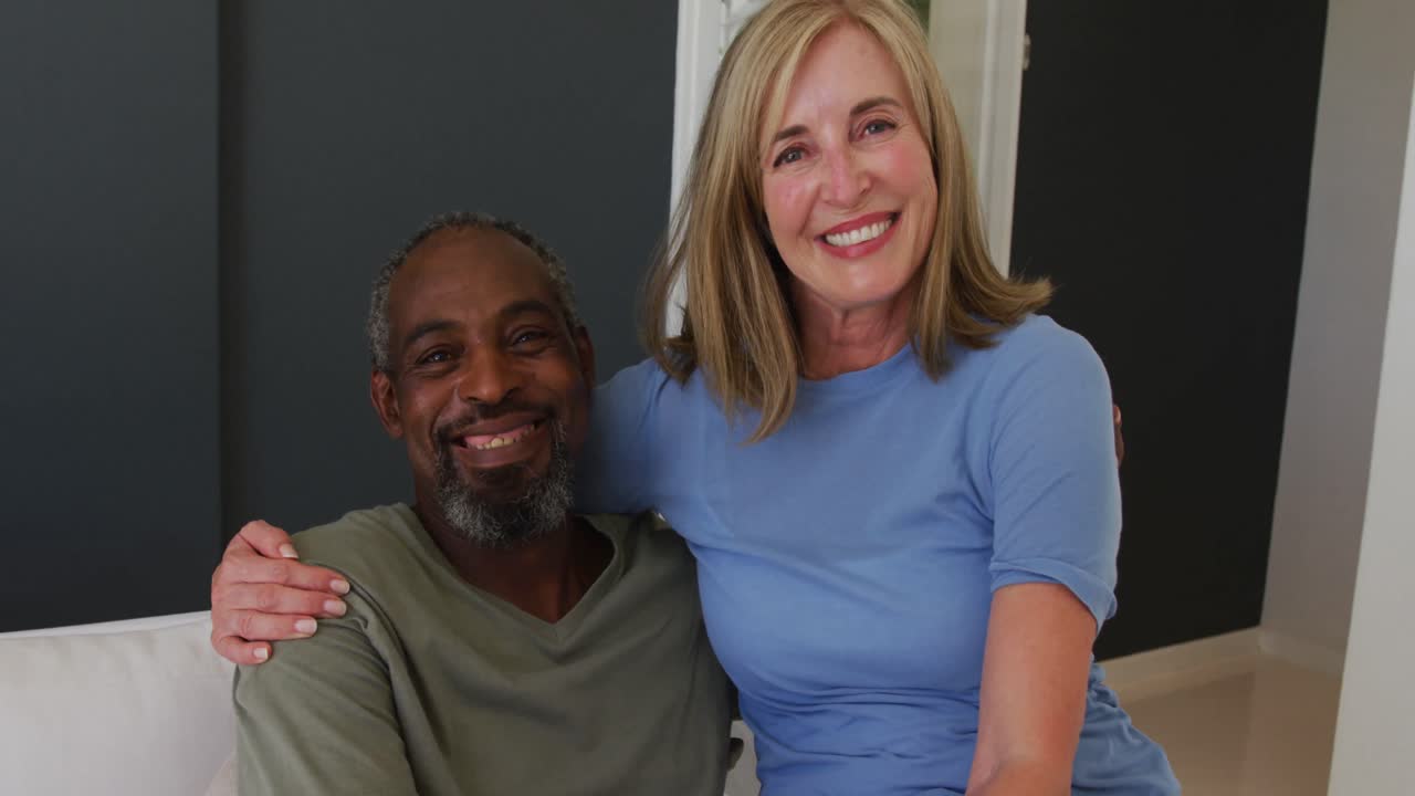 Portrait of mixed race senior couple smiling while sitting on the couch at home