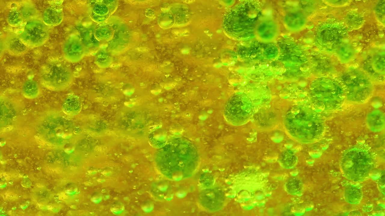 Close-up view of green bubbles forming and moving in a yellow liquid, creating a dynamic visual effect.