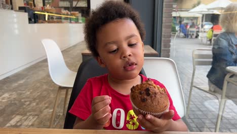 Niño-Negro-De-3-Años-Saboreando-Un-Muffin-De-Chocolate:-Una-Delicia-Alegre-Dentro-De-Una-Cafetería