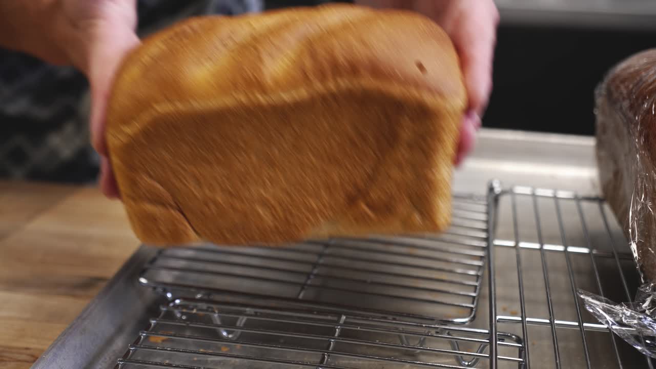 Baker sets freshly baked white country loaf on cooling rack, slow motion 4K