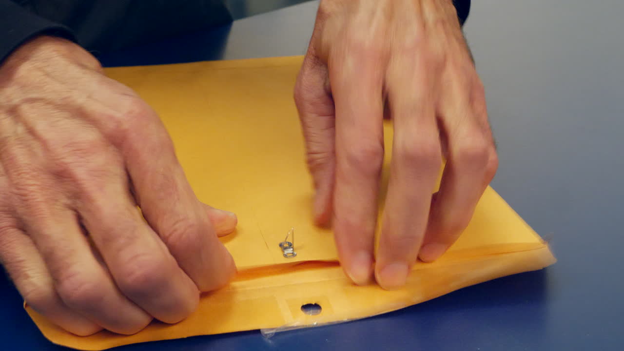 우송 및 배달된 후 내부에 중요한 문서가 들어 있는 주황색 봉투를 여는 손 클로즈업 슬라이드 왼쪽