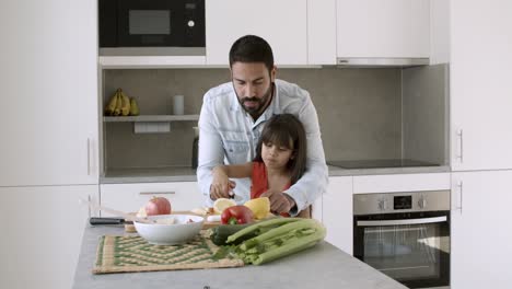 dad helping little daughter to cut vegs