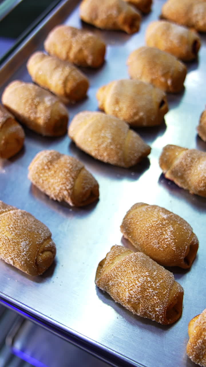 Freshly baked pastry on baking sheets are piled on shelves. Croissants and bagels production at bakery. Close up. Vertical video