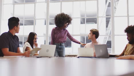 millennial black female manager stands addressing coworkers in a meeting room, low angle view