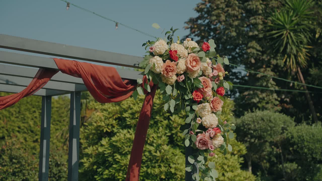 Beautiful pergola decorated with roses, hydrangeas and rust colored fabric for ceremony
