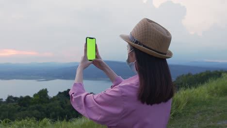 handheld shot : woman tourist holding a green screen phone at night and a woman wearing a mask to prevent disease.