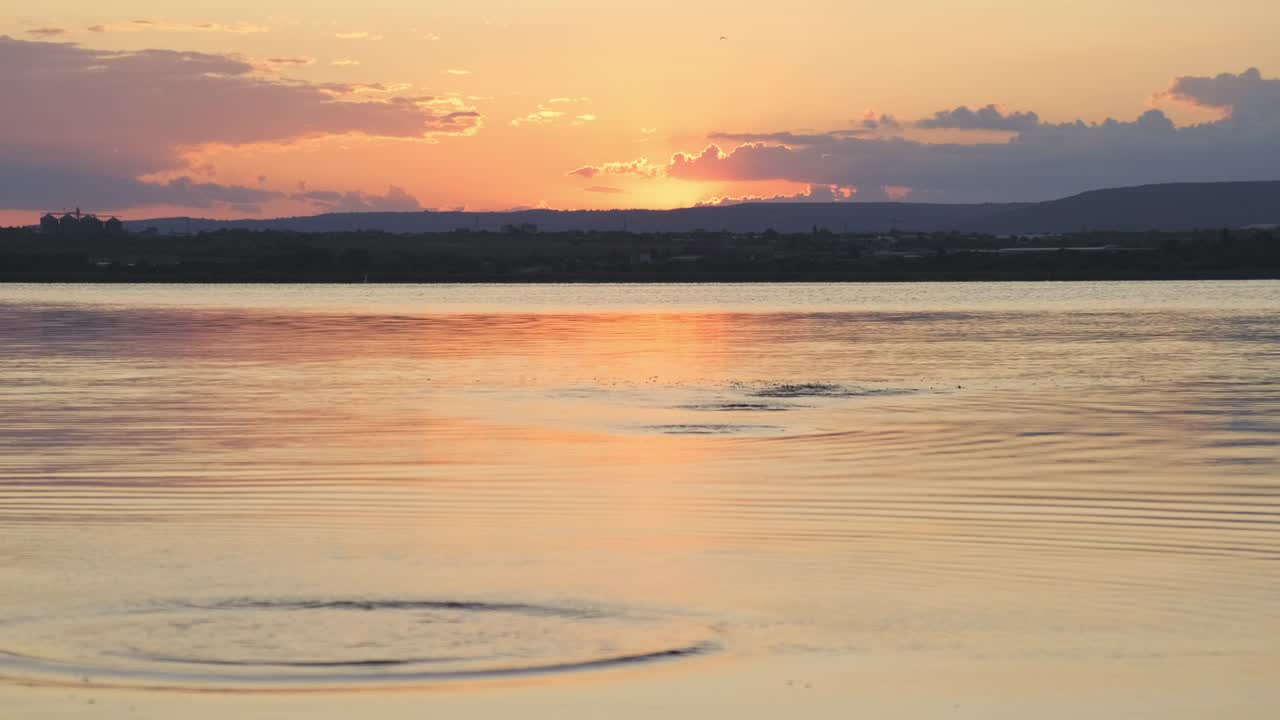 Abandoned stones in sea and circles from them on surface of water. Calm surface of sea water. Texture is small ripple. Calm sea background against a bright, orange sunset