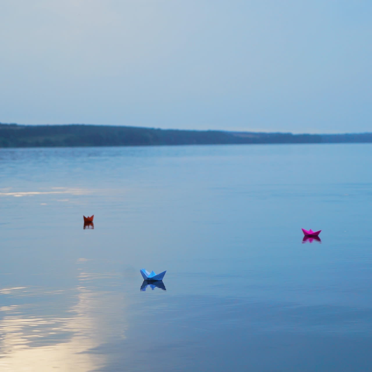 Beautiful evening scenery of a calm river and colored paper boats on water background. Four origami ships floating at sunset