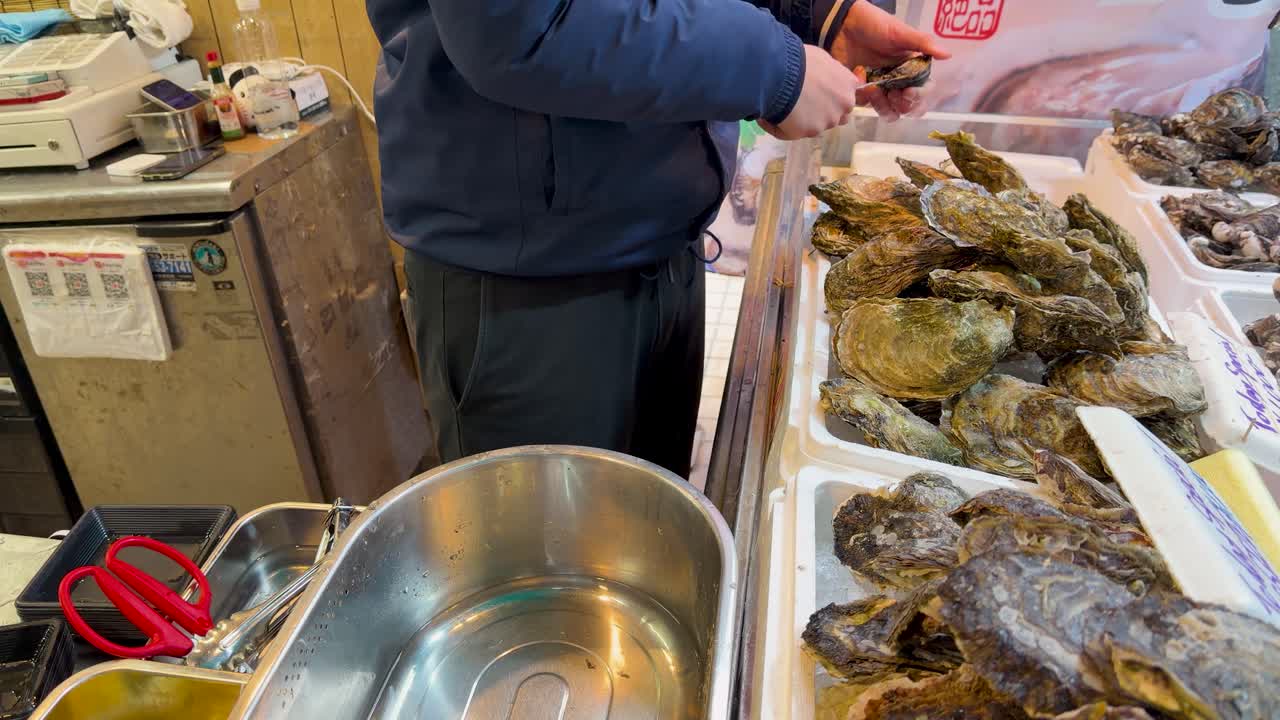 A close-up shot shows a vendor expertly shucking raw oysters at a Tokyo market