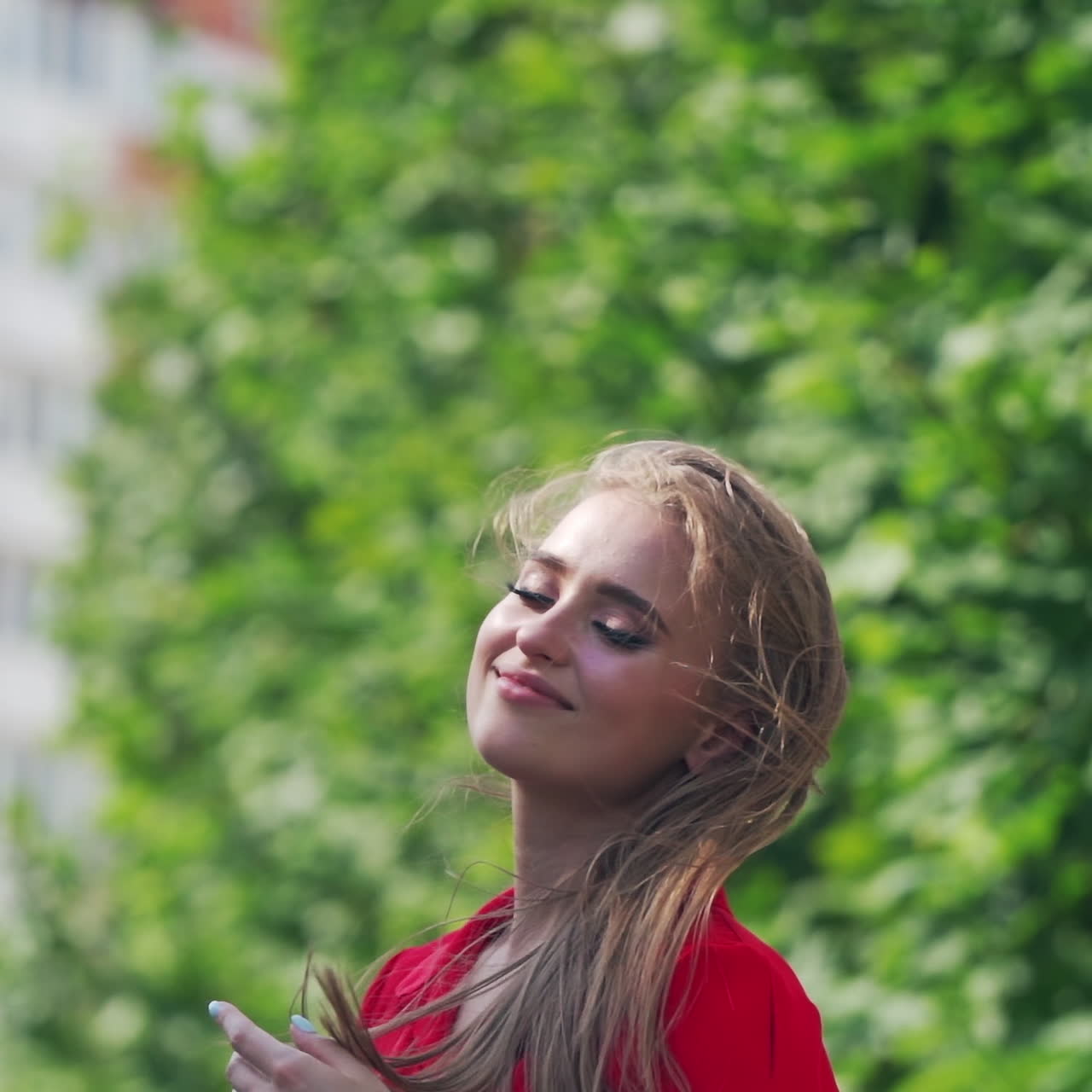 Beautiful smiling woman with long hair. Portrait of a gorgeous model in red clothing on green tree background. Happy attractive female outdoors.