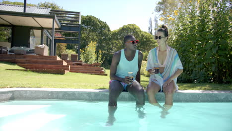 diverse couple sitting by pool, enjoying drinks and sunshine, at home, copy space