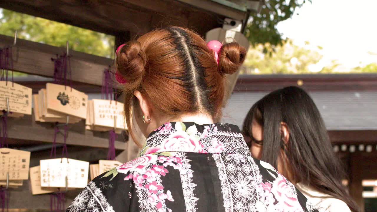 Plan moyen d'une femme en kimono traditionnel regardant des plaques de prière en bois dans un sanctuaire.