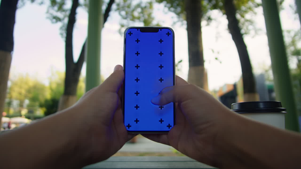Young woman holding and swiping phone chroma key screen in the park in front of trees close-up. Girl with green screen on smart phone. Nature