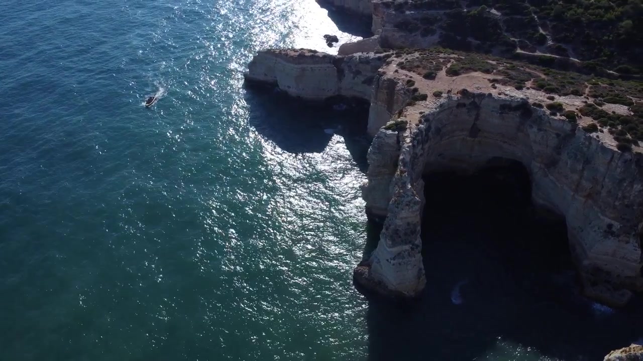 Experience the stunning natural beauty of Portugal's Algarve region. A boat glides across the vibrant blue ocean, exploring majestic sea caves and towering rock formations bathed in bright daylight.