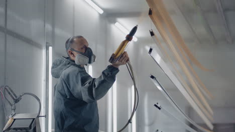 a man in a respirator is painting metal with a powder method.painting shop. the painter works with a spray gun paint is applied