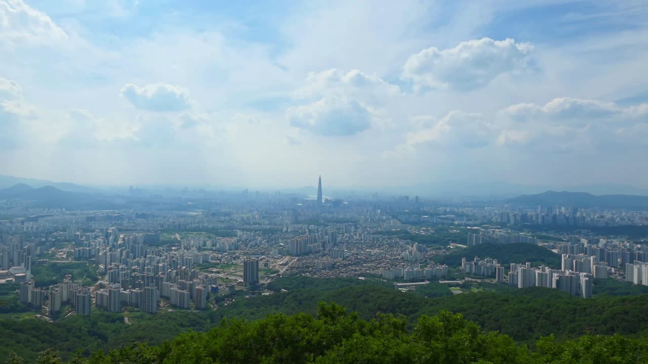A slow zoom-in shot captures the panoramic view of the sprawling metropolis of Seoul, South Korea, focusing on the iconic Lotte World Tower as seen from the historic Namhansanseong fortress