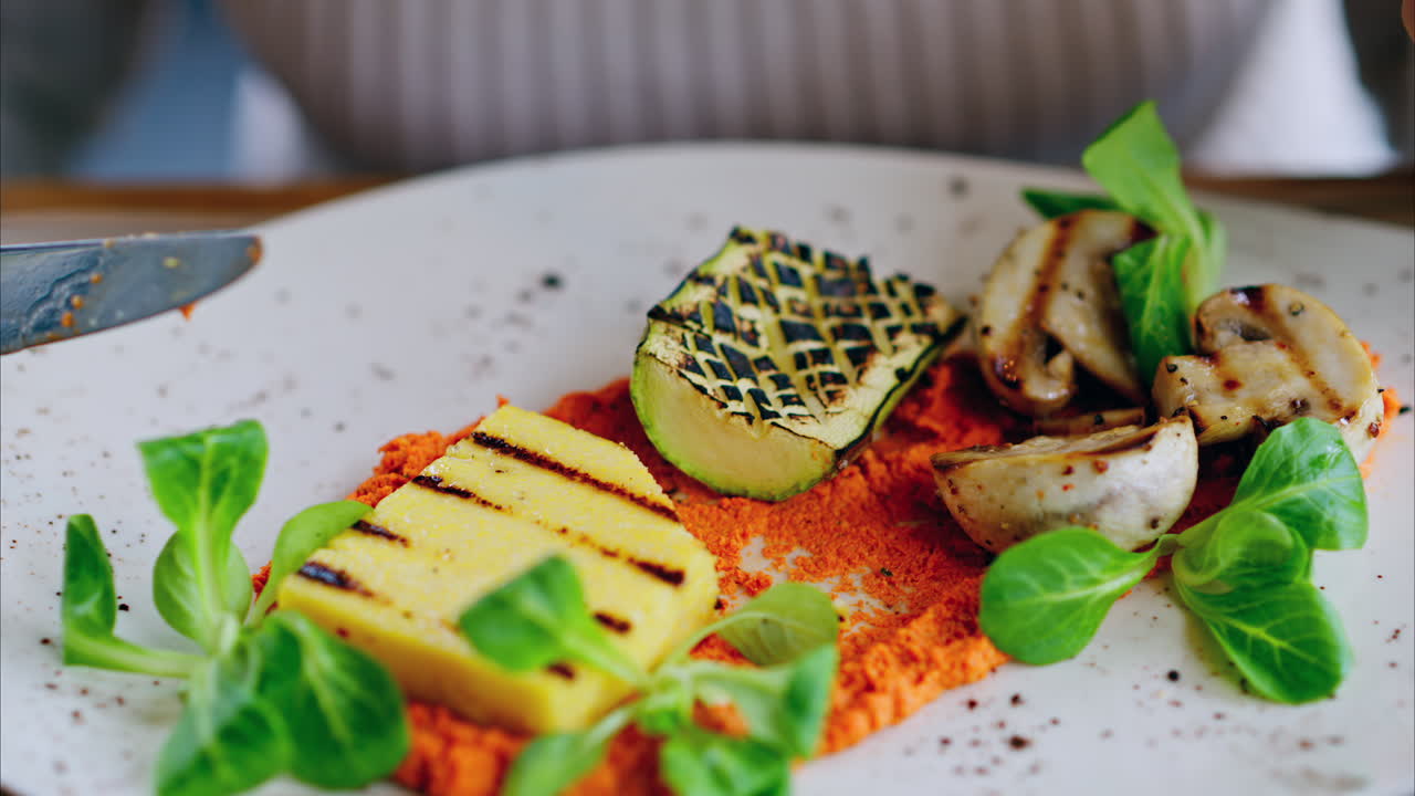 Woman eating grilled zucchini with mushrooms, polenta and hummus