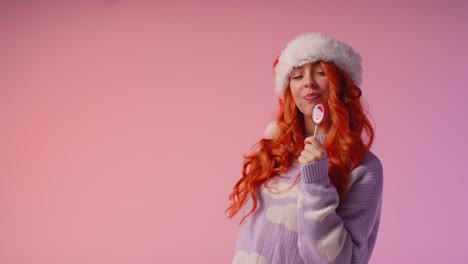 Studio-Portrait-Shot-Of-Young-Gen-Z-Woman-Wearing-Christmas-Santa-Hat-Holding-Candy-Lollipop-1