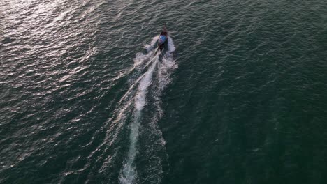 toma aérea de drones siguiendo un bote de cola larga a lo largo de la playa de ao nang, krabi, tailandia durante la noche