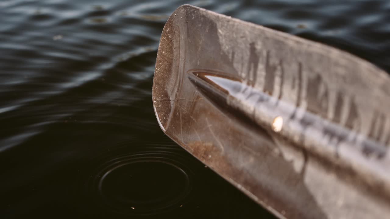 Close-up of a kayak paddle dripping water into a calm lake, with ripples forming where the drops meet the surface