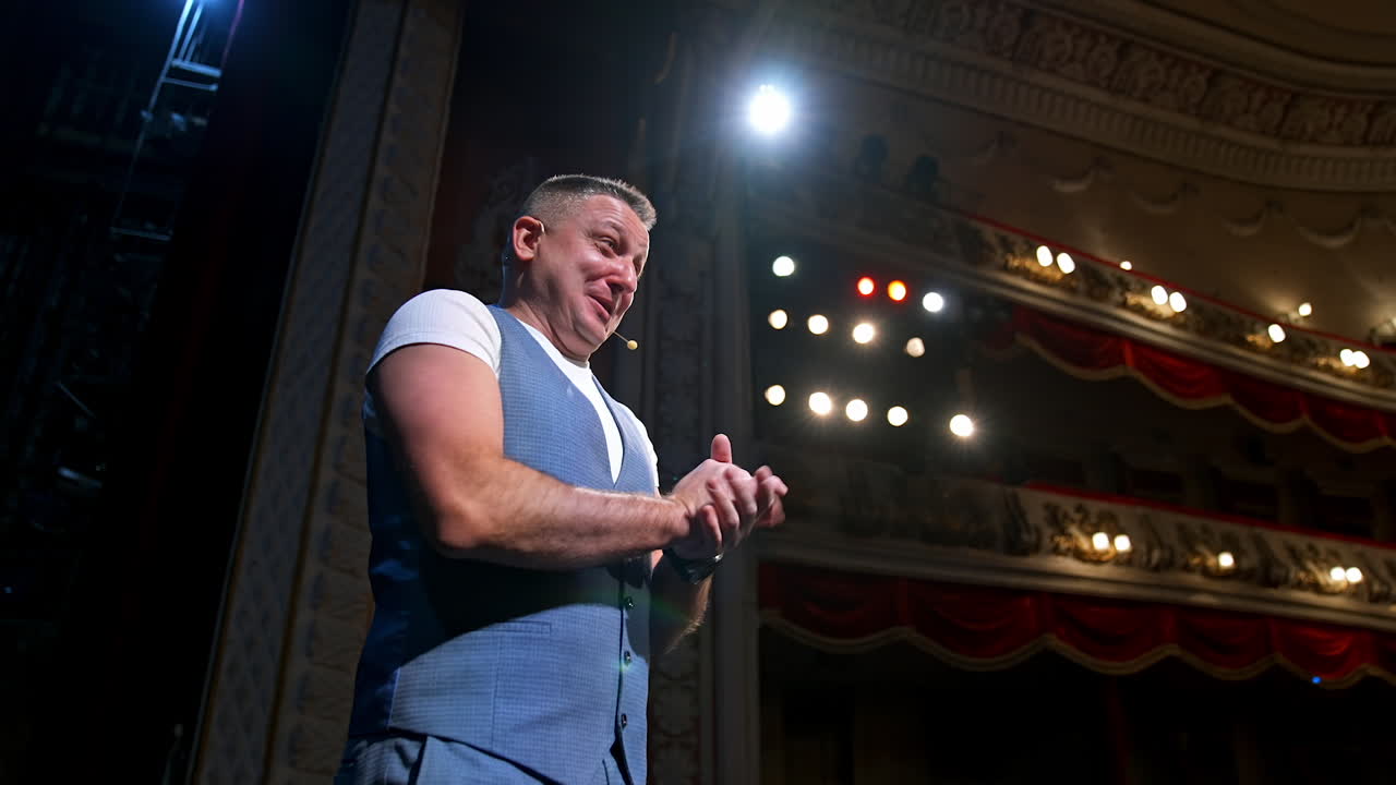 Comedian on stage. Middle-aged speaker standing on stage and talking to someone. Smiling actor rehearses on scene.