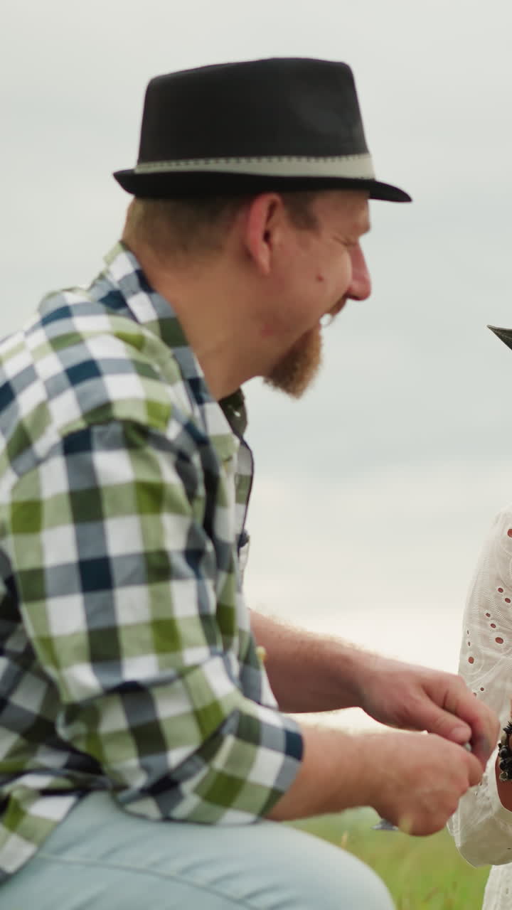 색 셔츠와 모자를 입은 장인 한 명이 페인트 튜브를 열기 위해 고군분투하는 동안, 색 드레스와 모자 입은 여자가 그의 노력에 웃는 유머러스한 장면