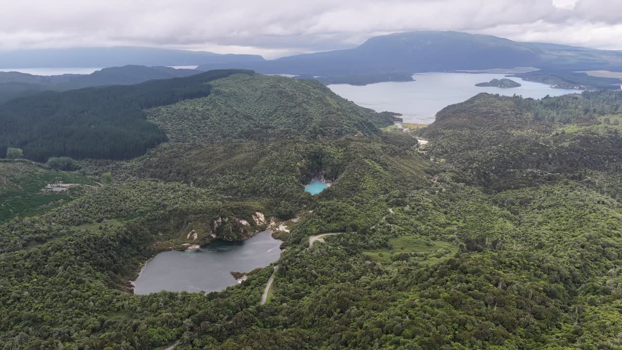 Vista aérea de exuberantes colinas verdes y lagos bajo un cielo nublado en un paisaje natural remoto.