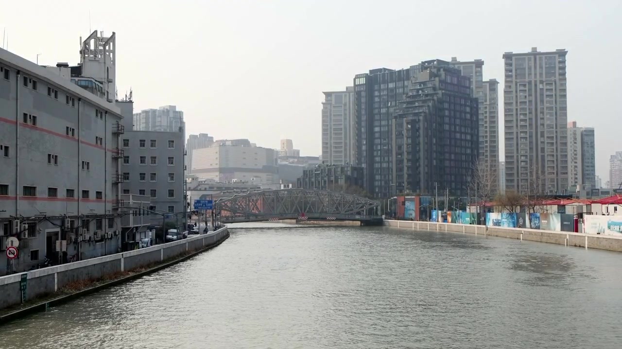 Canale urbano fiancheggiato da moderni grattacieli e strutture industriali a Shanghai, Cina, in una giornata fosca.