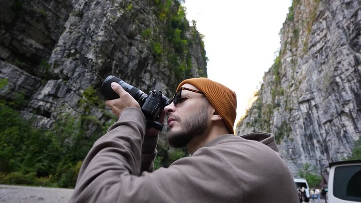 Bearded photographer taking photos of wild mountain forest nature with camera.