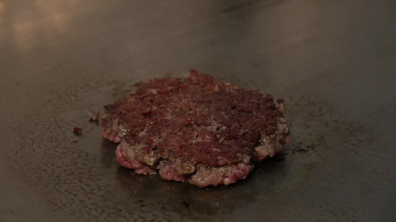 chef volteando hamburguesa con espátula y vierte un poco de sal mientras cocina en la estufa