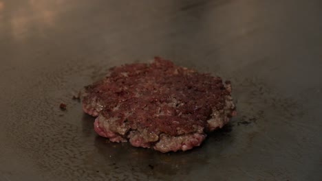 Chef-flipping-burger-patty-with-spatula-and-pours-some-salt-while-cooking-on-stove