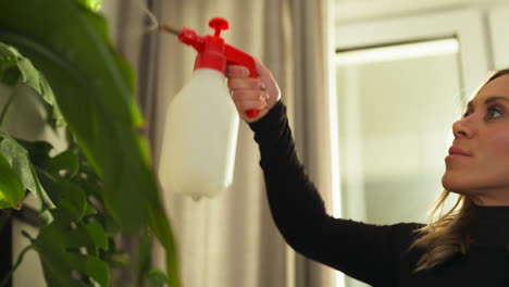 handheld shot of blond caucasian woman spraying water on plants at her home, interior