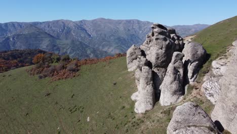 Mountain-aerial-flight-along-granite-outcrops,-autumn-colour-foliage