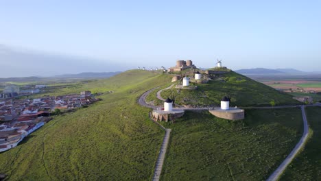 drone ascent revealing set of antique windmills and medieval castle on hilltop at sunrise